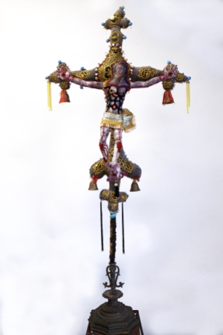 The Anchorite's Crucifix 2019 Mixed media: acrylic painted canvas, recycled fabric, beads, bells, embroidery floss, black pipe interior structure, poly-fil, vintage furniture, metal work and fabric. 60 by 32 by 10 inches, Crucifix only; total installation varies upon situation.